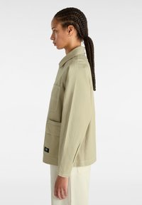 Chaqueta de utilidad verde claro con un ajuste relajado, bolsillo en el pecho y detalles de costura visibles. Fabricada con tela texturizada.