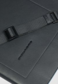 Superficie di borsa in pelle nera con tracolla nera regolabile e nome del marchio "Piquadro" in rilievo.