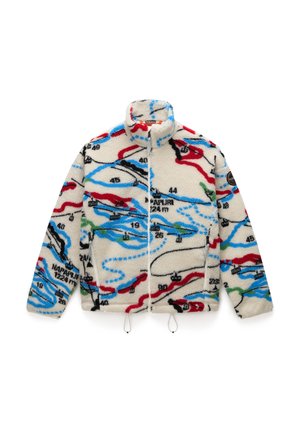 Fleeces jaka ar krēmkrāsas pamatni, ar daudzkrāsainām, kartēm līdzīgām rakstainēm sarkanā, melnā, zilā un zaļā krāsā; tai ir augsts apkakle un rāvējslēdzēja aizdare.