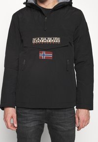 Sort pulloverjakke med en lynlåslomme, prydet med et stort mærket patch og et norsk flagaccent. Fremstillet af vandafvisende materiale.