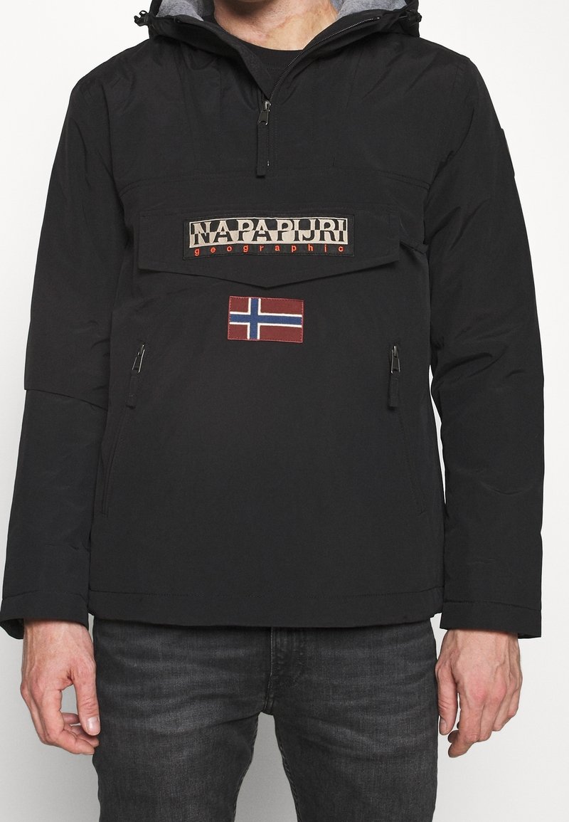 Sort pulloverjakke med en lynlåslomme, prydet med et stort mærket patch og et norsk flagaccent. Fremstillet af vandafvisende materiale.