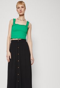Zöld, smockolt crop top fodros pántokkal, amelyhez egy fekete, gombos maxi szoknya tartozik, texturált anyagból és barna gombokkal.