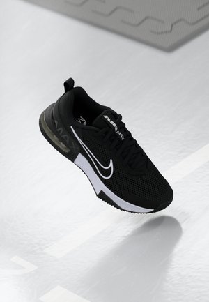 Baskets Nike Air Max noires avec logo swoosh blanc, tige en mesh, coussin d’air visible et semelle noire flottant au-dessus d’une surface blanche.
