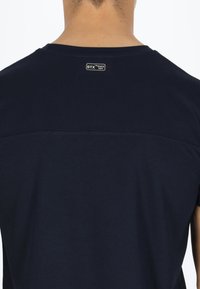 T-shirt blu navy realizzato in tessuto ad asciugatura rapida. Presenta un'area posteriore senza cuciture e un piccolo etichetta STX vicino al colletto. Texture morbida.