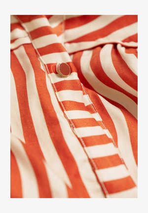 Gestreepte blouse met rode en crèmekleurige tinten, zachte stof, knoopdetails en zichtbare stiksels langs de knoopsluiting.