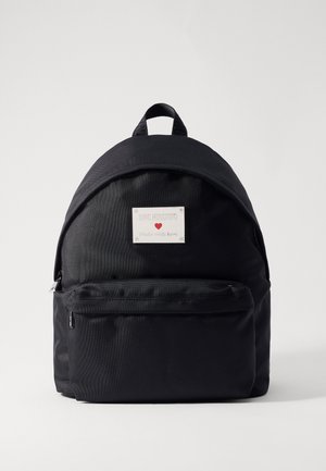 Czarny plecak materiałowy z przednią kieszenią na zamek i białą metką z napisem "LOVE MOSCHINO Made with love" z małym czerwonym serduszkiem.