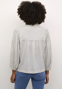 Blouse rayée en crème clair et noir, avec un dos froncé, des manches bouffantes et des poignets élastiques, fabriquée à partir d'un tissu doux.