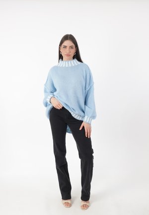 Suéter de punto azul claro con cuello alto y ribetes de rayas blancas, combinado con jeans negros de pierna recta y sandalias beige.