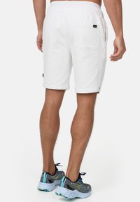 Hvide bomuldsshorts med elastisk talje, sidelommer og en baglomme. Båret med grå sportsko med blå detaljer.