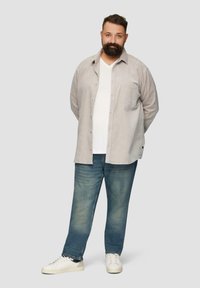 Grauhemd mit Knöpfen, über einem weißen V-Ausschnitt T-Shirt getragen, kombiniert mit blauen Jeans und weißen Sneakers. Lässiger Schnitt mit einer Taschenöffnung.