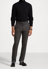 Czarny sweter z wysokim kołnierzem w splotem warkoczowym, zestawiony z dopasowanymi, szarymi wełnianymi spodniami o płaskim kroju oraz czarnymi mokasynami z subtelną kokardką.