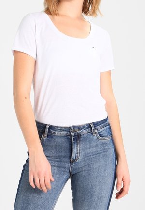 Osoba w prostym białym t-shircie z krótkim rękawem i niebieskich dżinsach na jasnym tle.