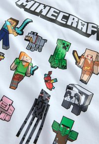 T-shirt blanc présentant des personnages pixélisés de Minecraft dans diverses couleurs, y compris un creep vert, un personnage bleu avec une épée et un perroquet rouge.