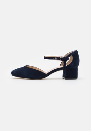 Navy blue suede heeled shoe with a pointed toe, ankle strap, and a square block heel. Smooth texture with a cutout design on the side.