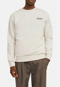 Sudadera de cuello redondo en color blanco roto con puños y bajo acanalados. Presenta texto de logo negro en el pecho. Textura suave y corte relajado.