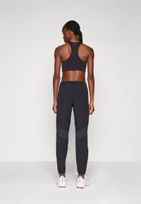 Černá sportovní podprsenka s designem racerback v kombinaci s černými zúženými kalhotami, které mají šedé kontrastní pruhy a zipy na kotnících.