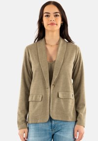 Blazer beige con tejido texturizado, dos bolsillos frontales y cierre de un solo botón. Presenta un cuello chal y mangas largas.