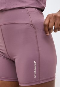 Κοντινό πλάνο ενός ατόμου που φοράει αθλητικό σορτς μωβ με το κείμενο «τρέξε με το μυαλό» και χέρι που τραβάει την πλαϊνή τσέπη.