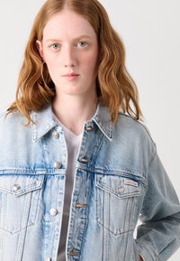 Lichtblauwe spijkerjack met een knoopsluiting aan de voorkant, twee borstzakken en een Calvin Klein logo label. De stof heeft een licht versleten textuur.