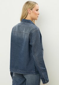 Donkerblauwe spijkerjack met een gradientontwerp, voorzien van een gespikkeld textuur op de mouwen en een klassieke kraag, met een losse pasvorm.