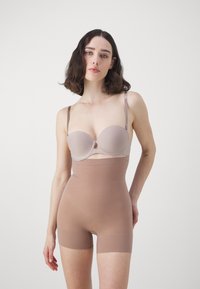 Beige strapless bra with molded cups paired with a high-waisted, nude bodysuit shorts, featuring a smooth, seamless texture.