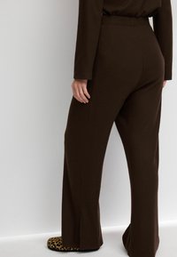 Pantalones amplios de canalé marrón con cintura alta y acabado texturizado, combinados con zapatillas de leopardo. Vista desde atrás.