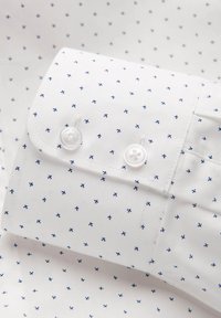 Camicia bianca con un sottile motivo a rete blu navy, dotata di polsini button-down con due bottoni bianchi e una texture di tessuto in cotone liscio.