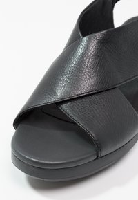 Sandal in pelle nera con un design a fascia incrociata e punta aperta. La suola è texturizzata e in stile platform per maggiore altezza.