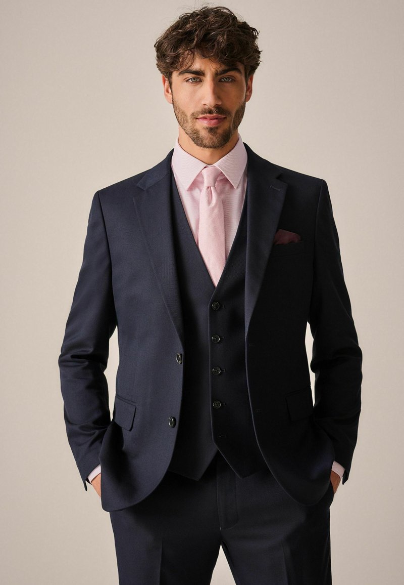 Marine pak met notch-lapels, colbert, en bijpassende broek. Roze gecheckerd overhemd en stropdas, met een pochet in de borstzak. Gevoeliger stof.
