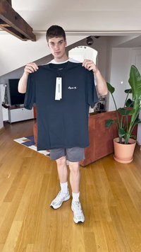 Camiseta de algodón negra de manga corta y cuello redondo, que presenta el texto "Royalty Co." en blanco, mostrada por una persona en interiores.