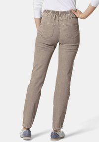 Hellbraune Jeans mit elastischem Bund, zwei Gesäßtaschen und geradem Bein-Schnitt, kombiniert mit grau-weißen Schuhen.