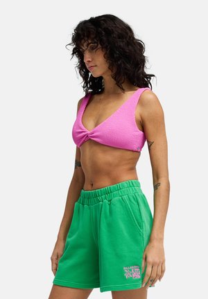 Roze gebreide bralette met brede bandjes en een gedraaide voorkant, gecombineerd met groene katoenen shorts met een elastische tailleband en logoprint.