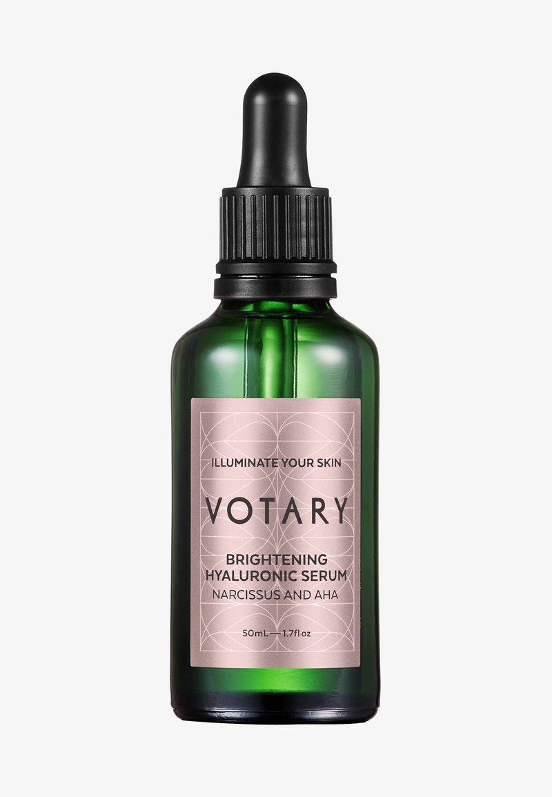 Grön glasflaska med en svart droppkork, har en rosa etikett med svart text som beskriver "Votary Brightening Hyaluronic Serum, 50mL."