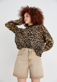 Suéter de estampado de leopardo en marrón y negro con cuello redondo. Combinado con pantalones cortos de tiro alto color beige, que cuentan con un cierre de botón en la parte frontal.