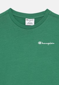 Πράσινο T-shirt Green Champion με στρογγυλή λαιμόκοψη, λευκό κεντητό λογότυπο στο στήθος και ετικέτα μεγέθους στο εσωτερικό του γιακα.