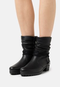 Botas de tobillo de cuero negro con parte superior arrugada, puntera redonda y tacón cuadrado. Presentan costuras gather y un cierre de cremallera lateral.