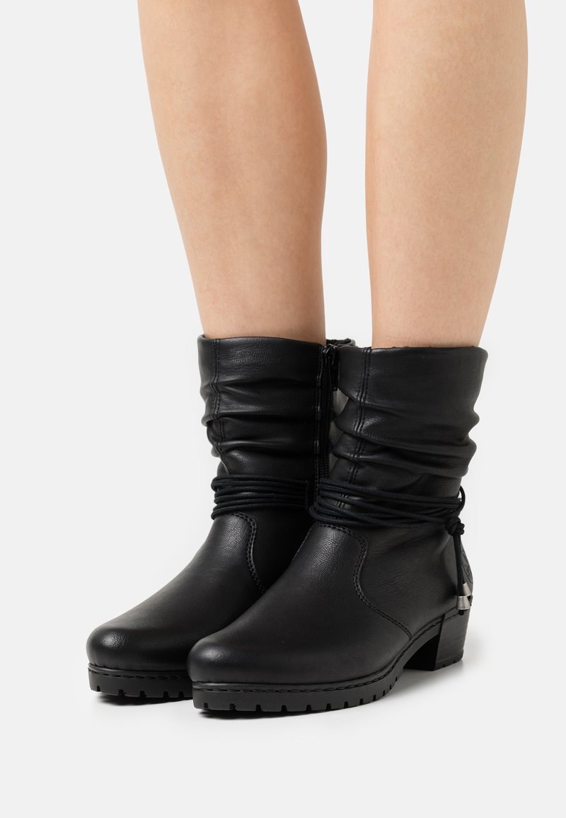 Botas de tobillo de cuero negro con parte superior arrugada, puntera redonda y tacón cuadrado. Presentan costuras gather y un cierre de cremallera lateral.