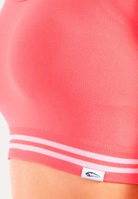 Reggiseno sportivo rosa in tessuto liscio, con scollatura tonda e dettagli a righe bianche lungo il bordo inferiore. Etichetta con logo visibile.