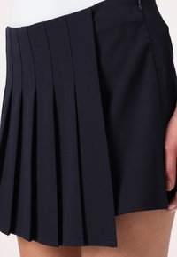 Navy pleated skirt made of smooth fabric, featuring a fitted waistband and vertical pleats extending from the waist to the hem.