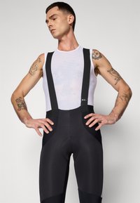 Shorts de vélo noirs avec bretelles texturées, une zone de siège rembourrée et un haut en mesh respirant. Comprend des accents cousus et un design ergonomique.