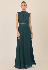 Teal iltapuku, jossa on istuva pitsitoppi, scalloped-reunat ja untuvainen hame. Suunnittelussa on monimutkaisista pitsikuoseista ja korkea kaula-aukko.