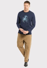 Granatowa koszula z długim rękawem z grafiką jasnoniebieskiego ośmiornica na środku, połączona z beżowymi spodniami cargo i czarnymi botkami.