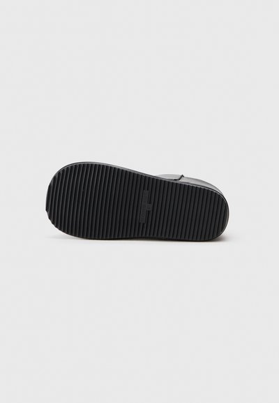 Soletta di scarpa in gomma nera con texture rigata, caratterizzata da un logo in rilievo e un bordo liscio. Il design è piatto e ampio per garantire stabilità.