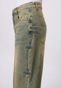 Falmede grønne denimjeans med en løs pasform, der har en frontlomme, baglomme og synlige slidmønstre langs stoffets side.