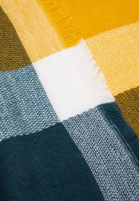 Cobertor tecido com um padrão cuadros em amarelo mostarda, branco, verde-água e verde escuro. Bordas texturizadas com acabamento desfiado.