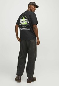 Black short-sleeve t-shirt featuring a large green and white graphic on the back. Paired with dark, loose-fitting pants and brown boots.