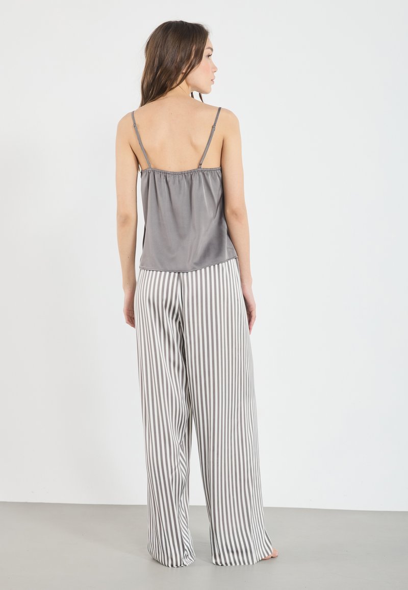 Débardeur en satin gris avec des bretelles fines, associé à un pantalon large à rayures verticales gris et blanches. Texture lisse et coupe décontractée.