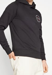 Sudadera negra de tela mezcla de algodón, con un pequeño logo en forma de corazón en el pecho, mangas largas y un acabado texturizado.