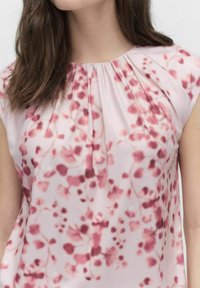 Kortärmad blus i mjukt, lätt tyg med ett rosa och vinrött blommönster och insamlingsdetalj vid halsringningen.