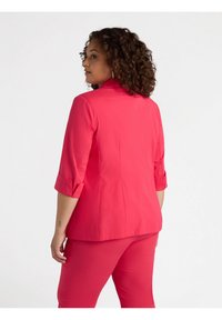 Giacca rosa con colletto, maniche arrotolate e dettagli di apertura sul retro. Realizzata in tessuto leggero con una texture liscia.